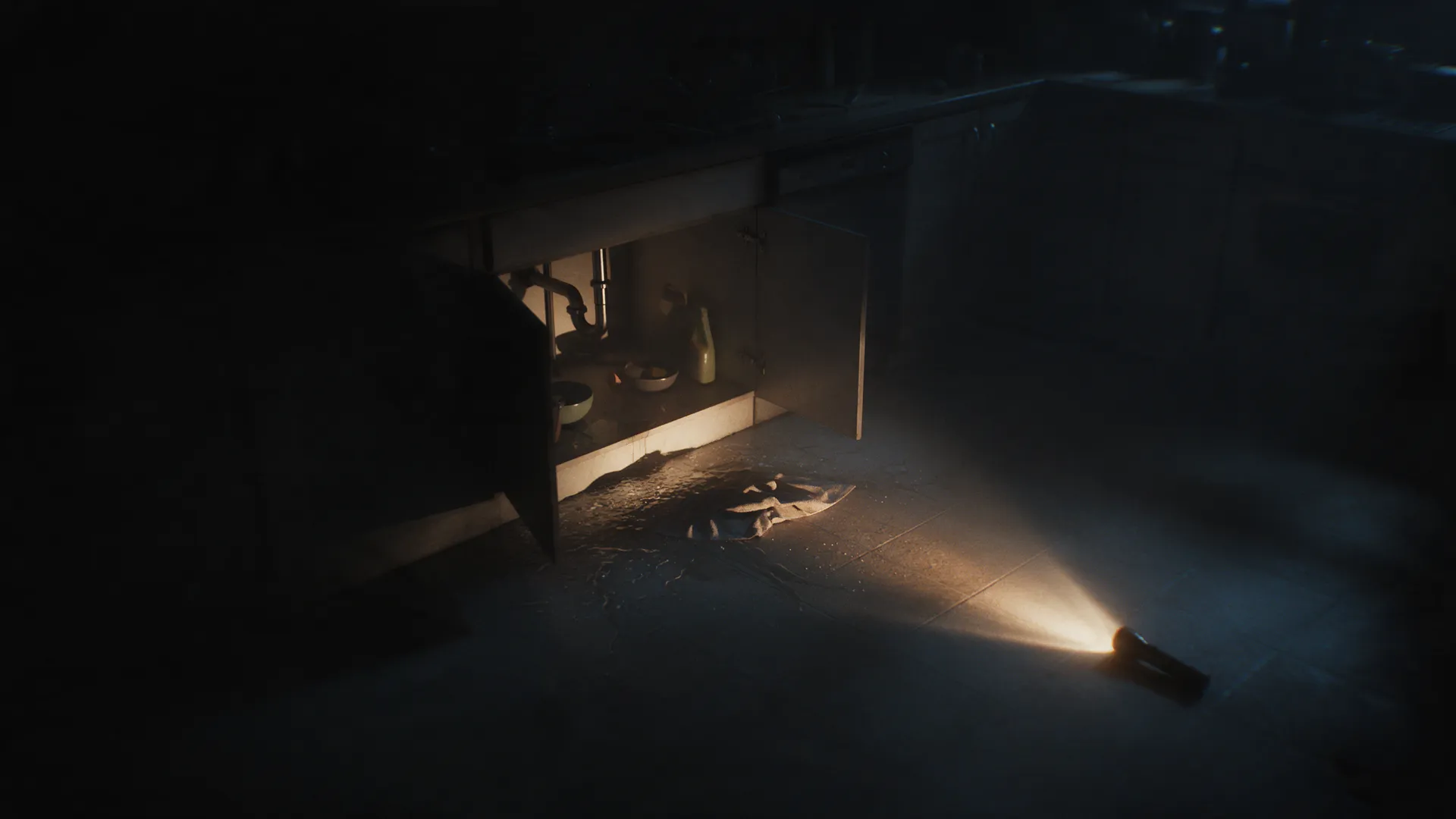 A kitchen at night lit by a flashlight on the floor, water spreading from under the sink cabinet.